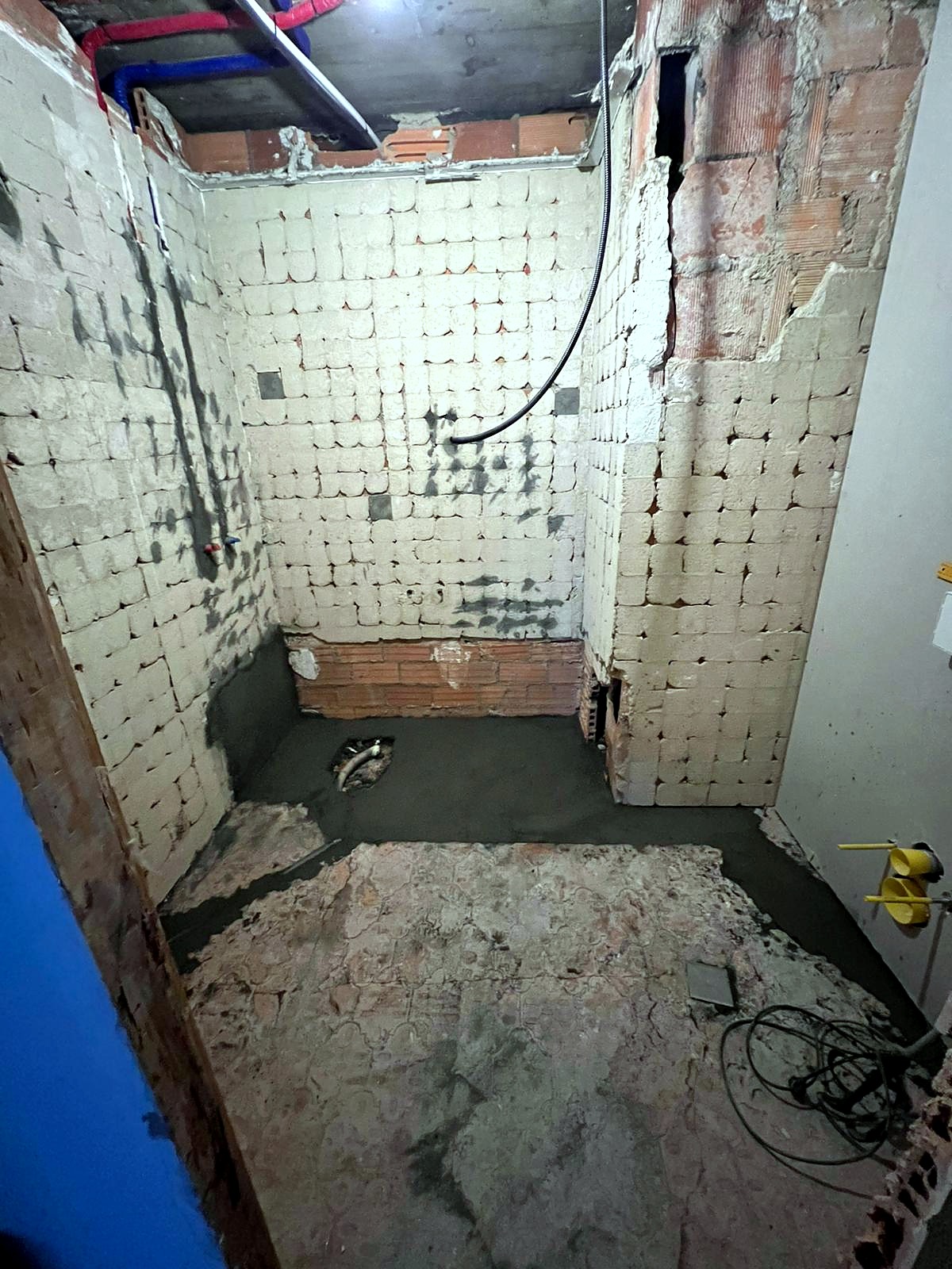 Baño en Ourense en estado inicial: paredes picadas con ladrillo a la vista, tuberías expuestas, suelo levantado, listo para reforma integral