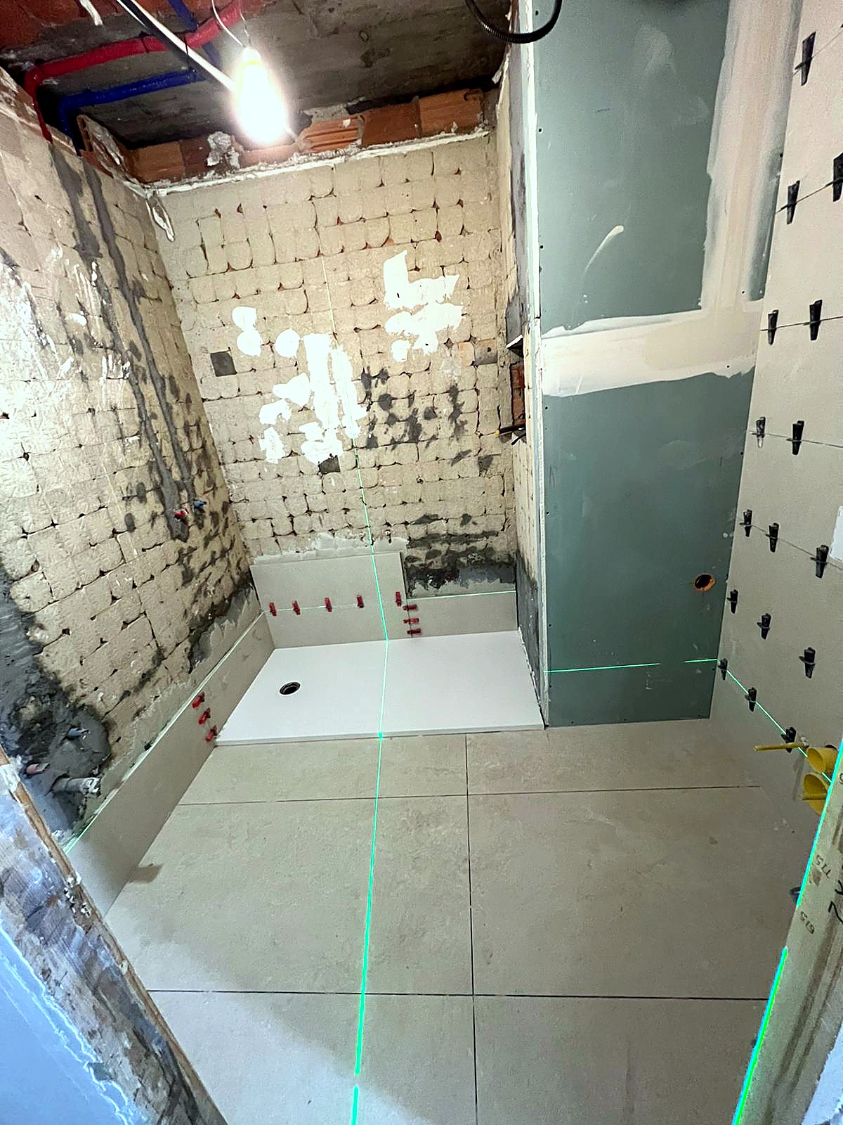 Replanteo de reforma de baño con láser de líneas verde: plato de ducha provisional, pared con pladur hidrófugo verde y crucetas de alicatado preparadas