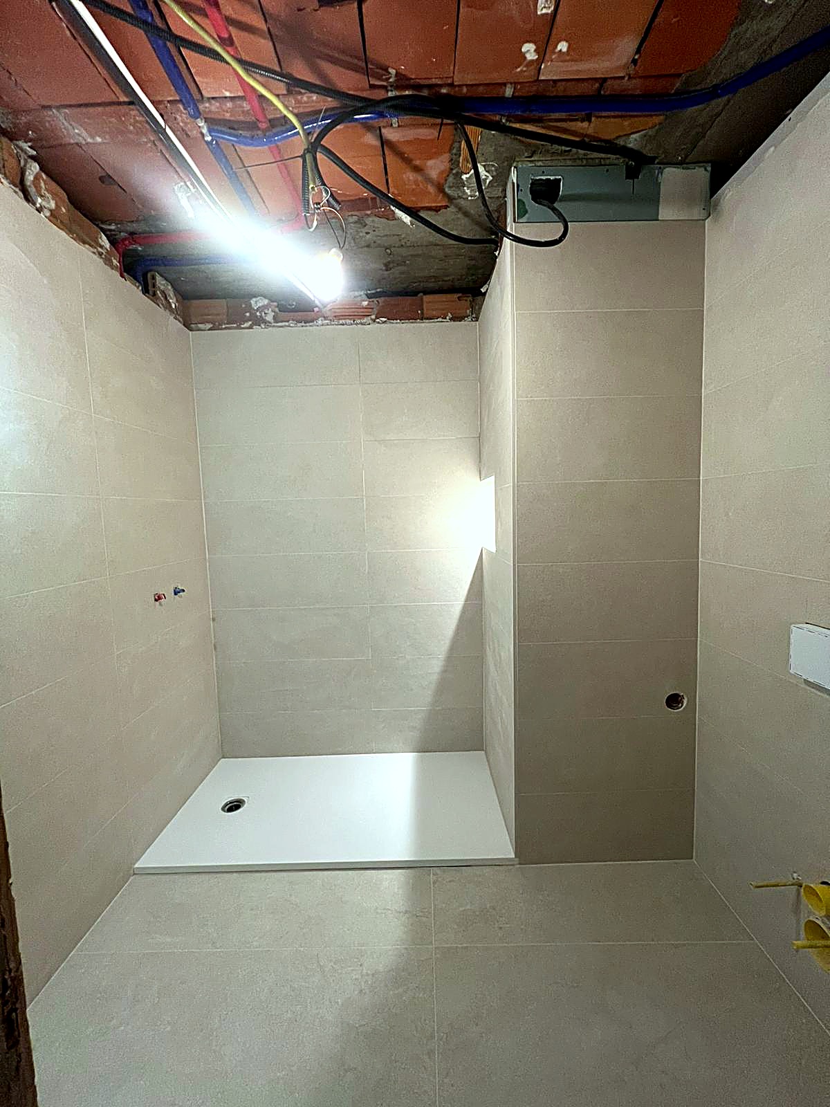 Baño en Ourense con alicatado terminado en gres porcelánico tono piedra, plato de ducha extraplano blanco, tomas de fontanería en pared para grifería empotrada