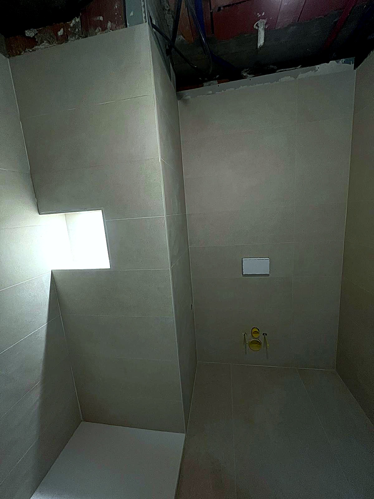 Hornacina dentro de la ducha con tira LED integrada y cisterna empotrada Geberit con pulsador rectangular blanco, alicatado en gres porcelánico continuo
